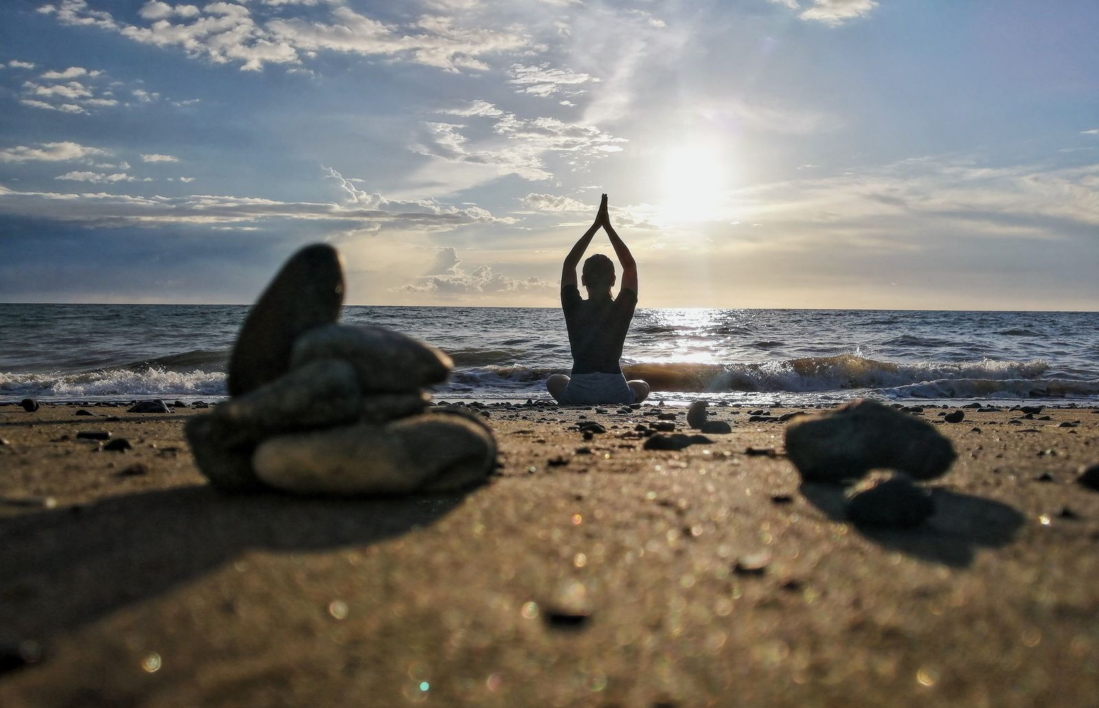 A person meditating in the lotus pose on a calm beach at sunset by the ocean