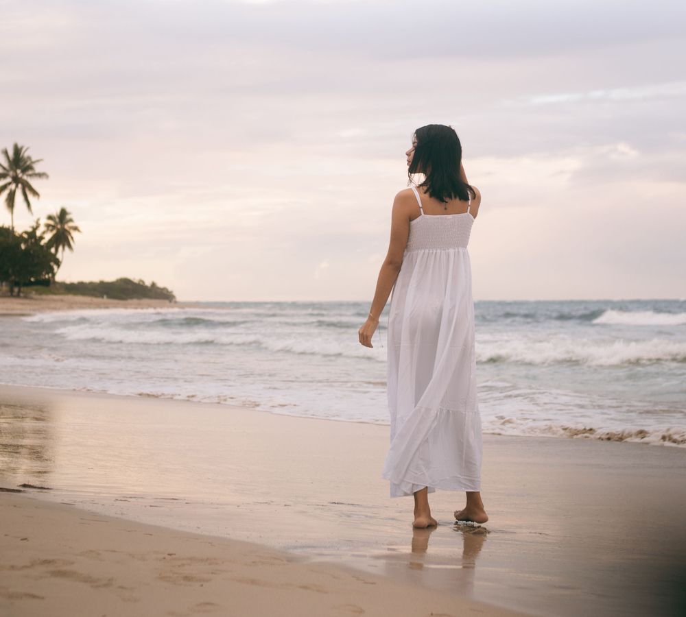 A woman in a white dress walking on the beach at sunset